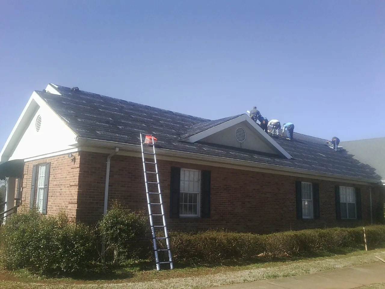 Crew tearing shingles off a brick ranch roof with a ladder set — Emergency Roof Repair work by our crew in Alva