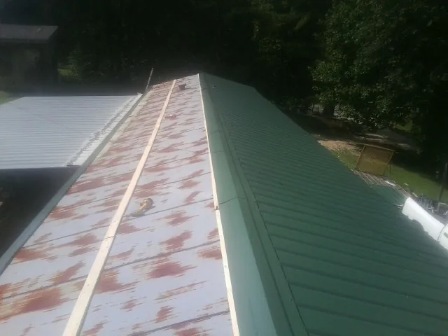 Old rusted panels beside newly installed green metal roofing — Wind Damage Roof Repair by Roofing Brothers in Alva