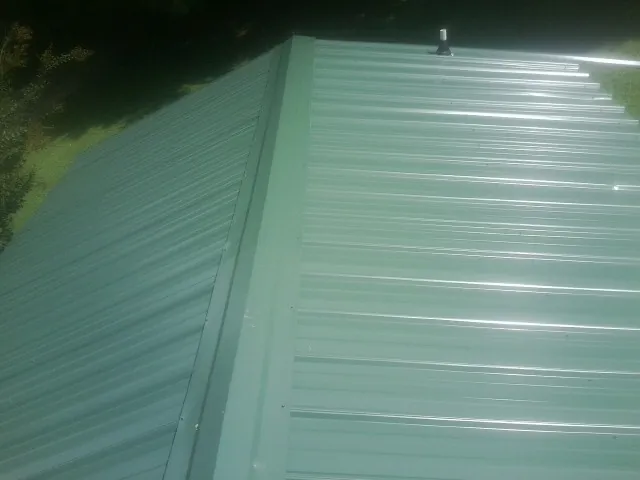 New green metal panels meeting at the ridge of a roof — Flat Roof Repair work by our crew in Alva