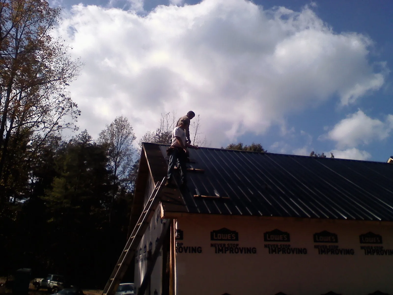 Roofer fastening dark metal panels high against a cloudy sky, from a Roof Inspection job in Alva