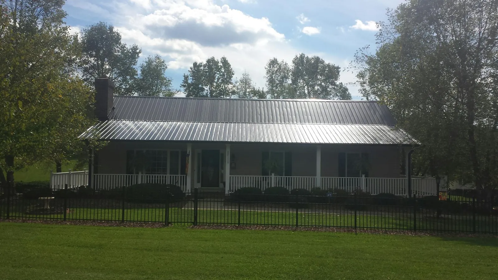 Gray metal roof on a brick ranch with a full width front porch — Gutter Guard Installation work by our crew in Alva